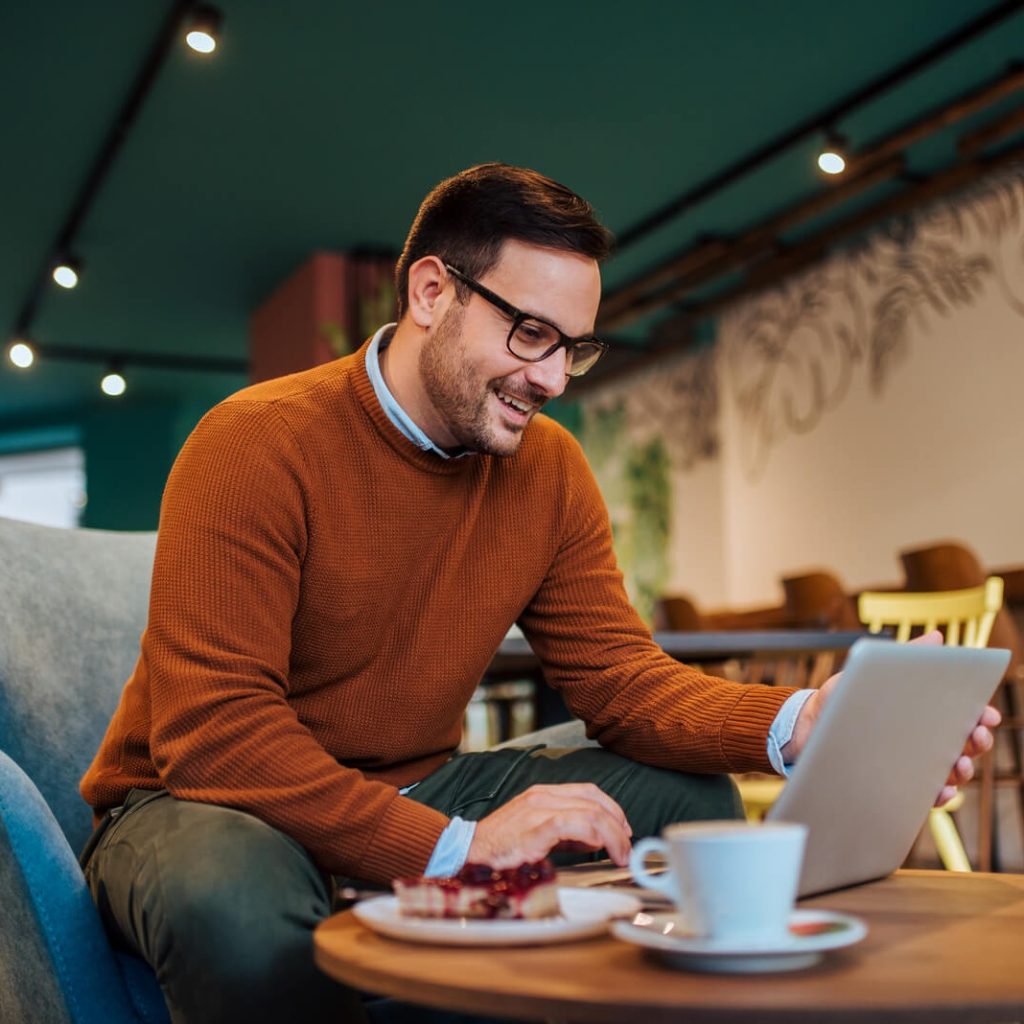 Cheerful Man Using Laptop In A Cozy Restaurant Po 2024 10 18 07 51 26 Utc 1 1 Cropped 1024x1024